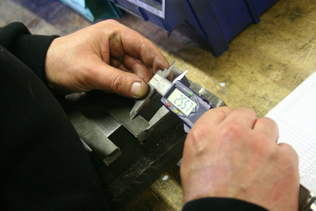 Inspector measuring a machined part with a digital caliper